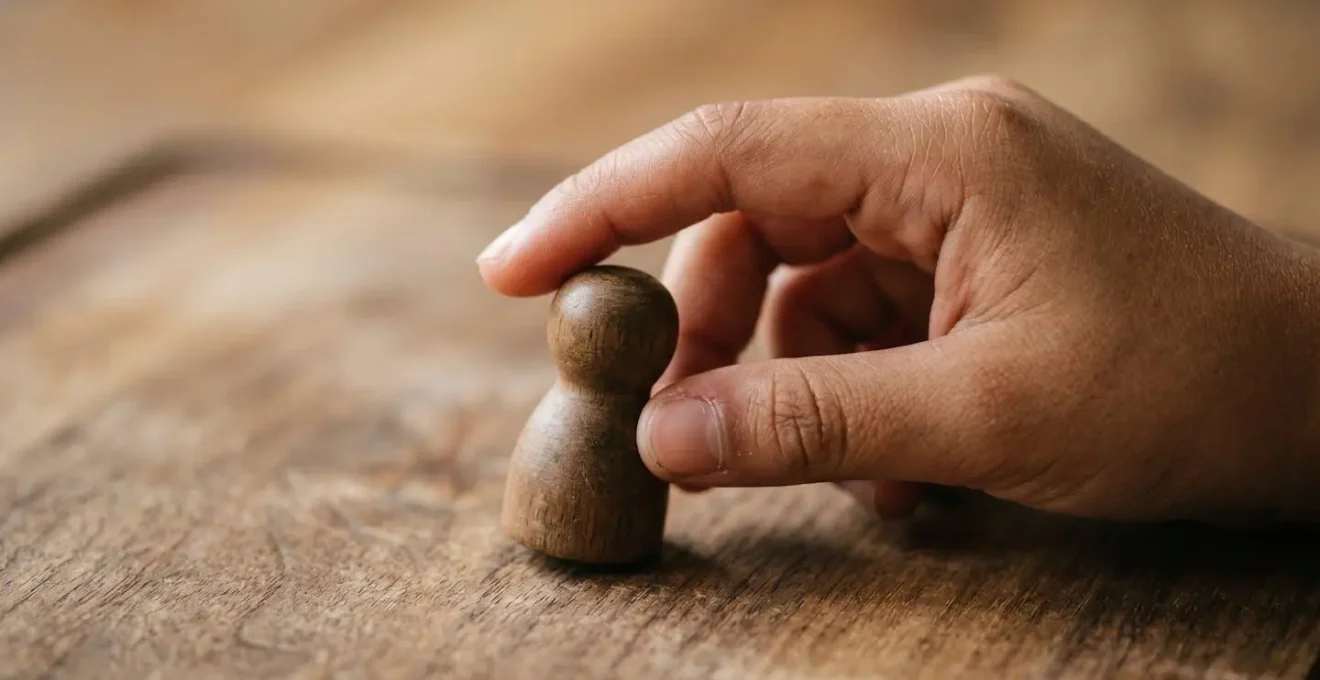 Extreme close-up macro view of a child's hand reaching for a game piece on a textured wooden board, showing patience and deliberate movement