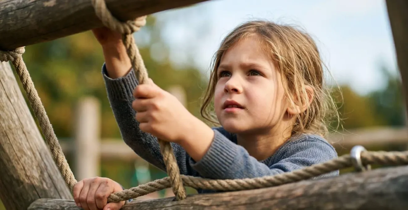 Close-up of a child's focused expression while climbing on natural playground elements