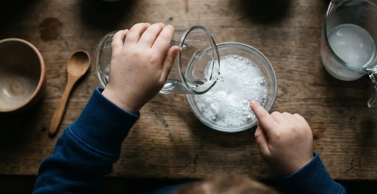 Young child's hands conducting a simple baking soda and vinegar science experiment with natural kitchen materials
